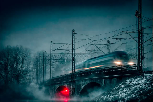 Wiadukt kolejowy w okolicach Dworca Wschodniego w Warszawie. Pociąg pędzi na wiadukcie kolejowym w mgle. Jest zima 2017 roku. 