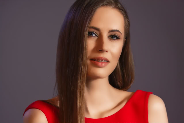 Urocze spojrzenie szatynki. Pociągła twarz. Modelka w czerwonej sukni. Zbliżenie twarzy. Kobieca sesja zdjęciowa. Portret Kobiety.