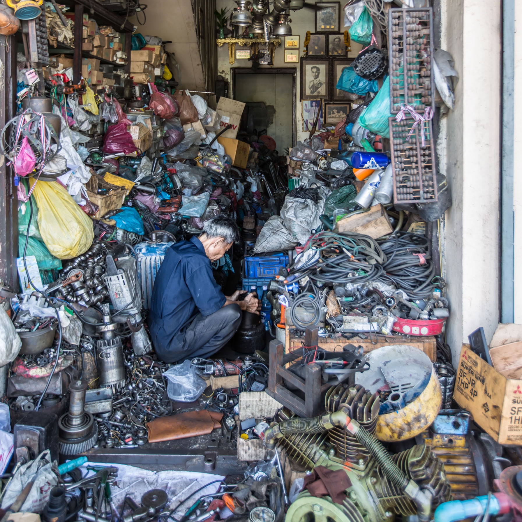 Starszy człowiek siedzi w otoczeniu różnych części zamiennych. Jest skupiony na naprawi silnika.
