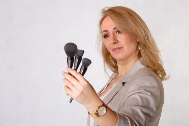 Profesjonalny portret kobiety trzymającej pędzle do makijażu, wykonany na jasnym tle, idealny do promocji makijażystki, usług beauty i marki osobistej. Portretowa Sesja Fotograficzna. Kobieca sesja zdjęciowa. Portret Kobiety.
